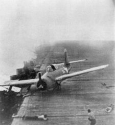 A Hornet Wildcat that just landed minutes earlier skids across Enterprise&rsquo;s flight deck as the carrier maneuvers violently during Junyo&rsquo;s dive bomber attack.  Two crewmen are taking defensive postures on the deck as smoke from earlier bomb hits swirls around them.