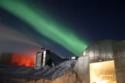 A full moon and 25-second exposure allowed sufficient light for this photo to be taken at Amundsen-Scott South Pole Station during the long Antarctic night. The new station can be seen at far left, the power plant in the center and the old mechanic's garage in the lower right. The green light in the background is the Aurora Australis.