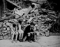 Children in the east end of London, made homeless by the random bombs of the Nazi night raiders, waiting outside the wreckage of what was their home. September 1940 (National Archives).